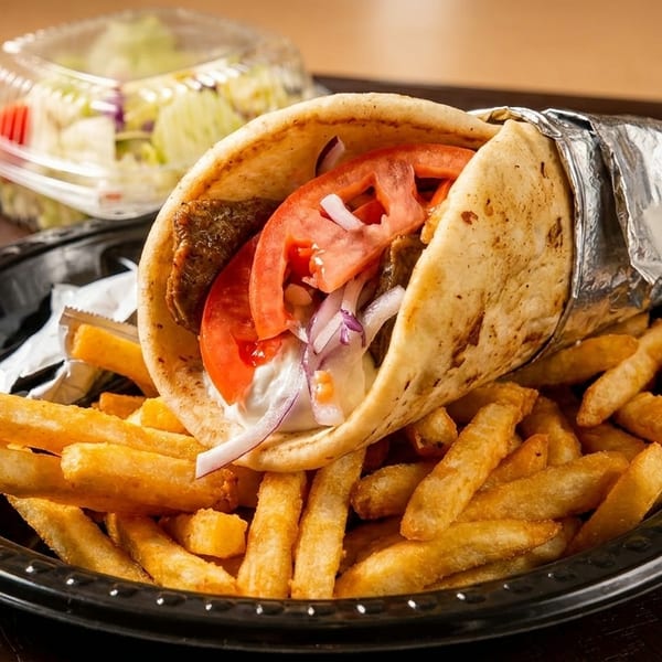 Gyro with meat, tomatoes, onions, and white sauce, served with golden fries and a side salad.